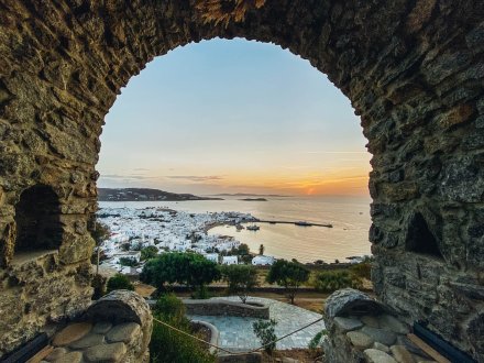 A view of Mykonos, Greece at sunset from an archway with views of the harbour, white town and mountains